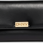 A luxurious and elegant close-up of a DKNY travel wallet and card holder in classic black. The image emphasizes the sleek design, meticulous stitching along the edges, and a subtly shimmering gold or silver metal DKNY logo. The material has a smooth, high-quality leather-like texture, suggesting a soft touch and refined craftsmanship. The lighting is soft and sophisticated, highlighting the rich quality of the product, perhaps resting on a dark, opulent surface. The overall impression is one of modern elegance and deep aesthetic appeal, hinting at an artfully designed accessory.